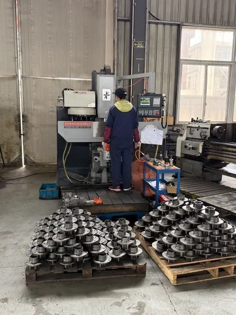 CNC vertical machining center in operation with stacks of precision-turned steel flange components on wooden pallets.