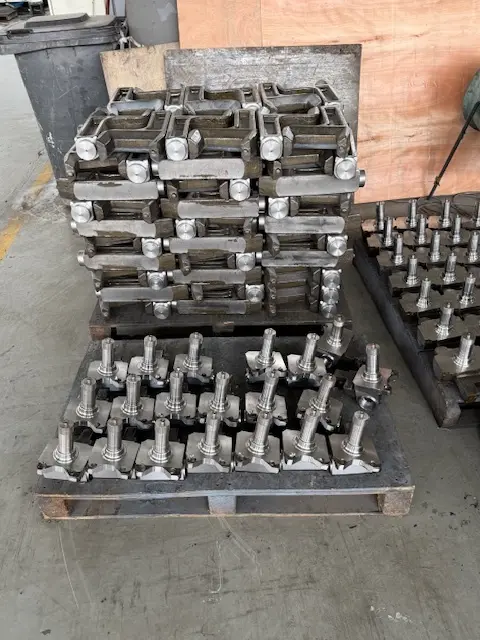 Pallets of CNC machined steel spindles and heavy-duty industrial hardware components organized in a metal fabrication shop.