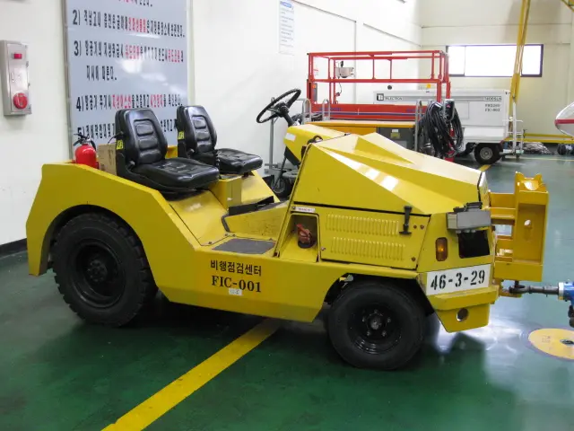 Yellow Harlan aircraft tug parked in a maintenance hangar, representing the global impact of specialized tractor engineering in international aviation logistics.