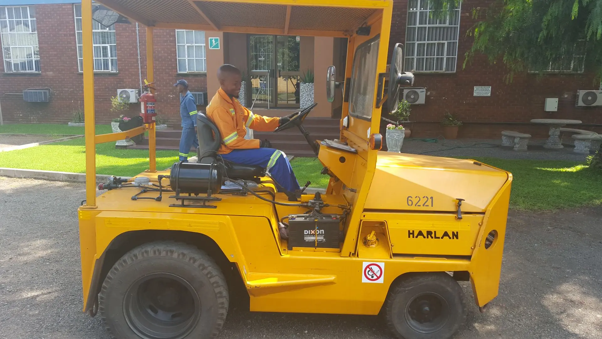 Worker operating a yellow Harlan industrial tractor in Cape Town, South Africa, demonstrating the global impact of specialized towing machinery in international logistics.
