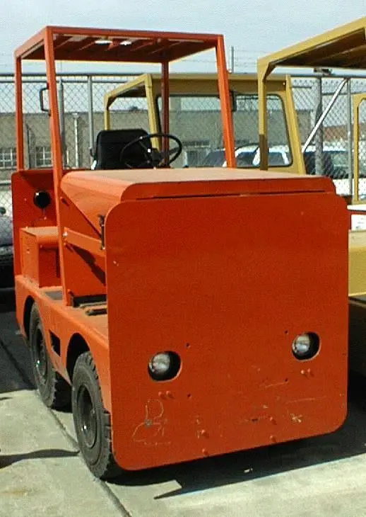 An orange Harlan electric baggage tractor featuring a protective overhead guard, illustrating heavy-duty craftsmanship and reliable performance in zero-emission airport ground handling.