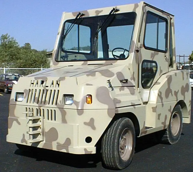 A high-capacity Harlan 16K tow tractor with a desert camouflage paint scheme and fully enclosed cab, engineered for specialized military aviation and heavy-duty industrial logistics.