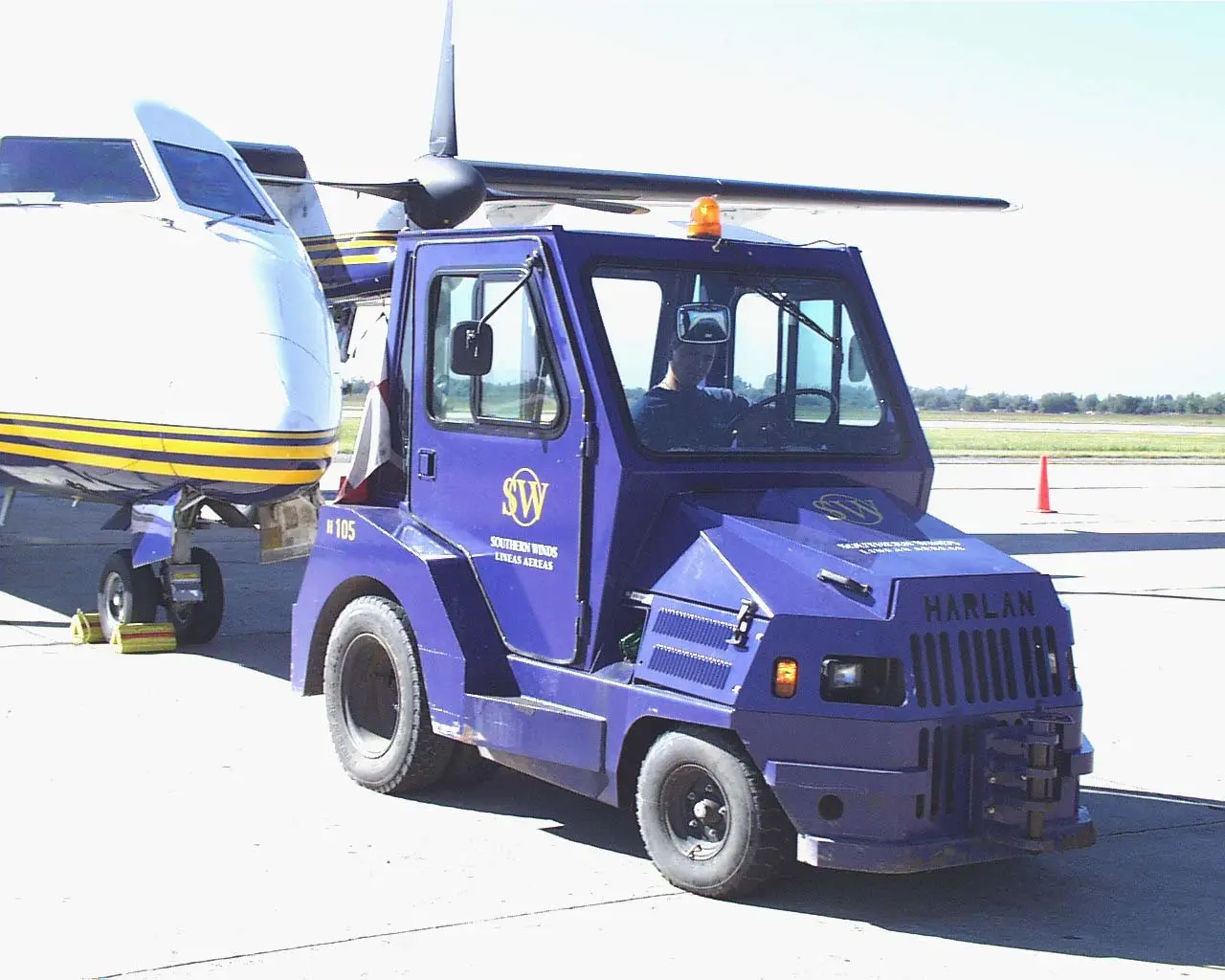 A classic blue Harlan aircraft tug with an enclosed cab in service for Southern Winds airlines, highlighting the long-term durability and specialized engineering of regional ground support vehicles.