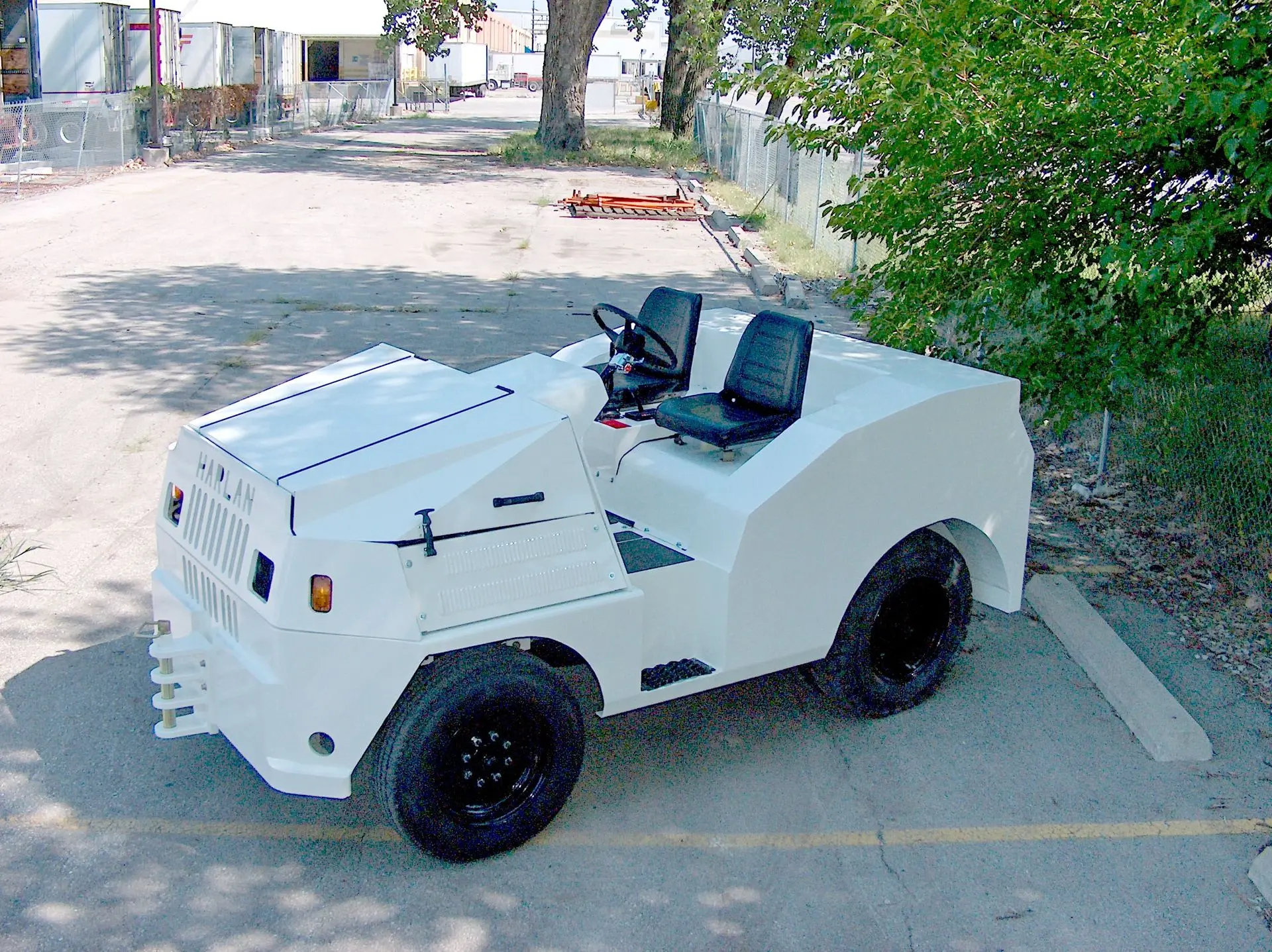 A high-performance white Harlan industrial tow tractor parked outdoors, demonstrating the advanced engineering and versatile design of modern airport ground support vehicles.